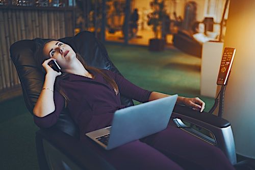 Eine Frau in einem Massagesessel telefoniert mit einem Computer auf den Beinen